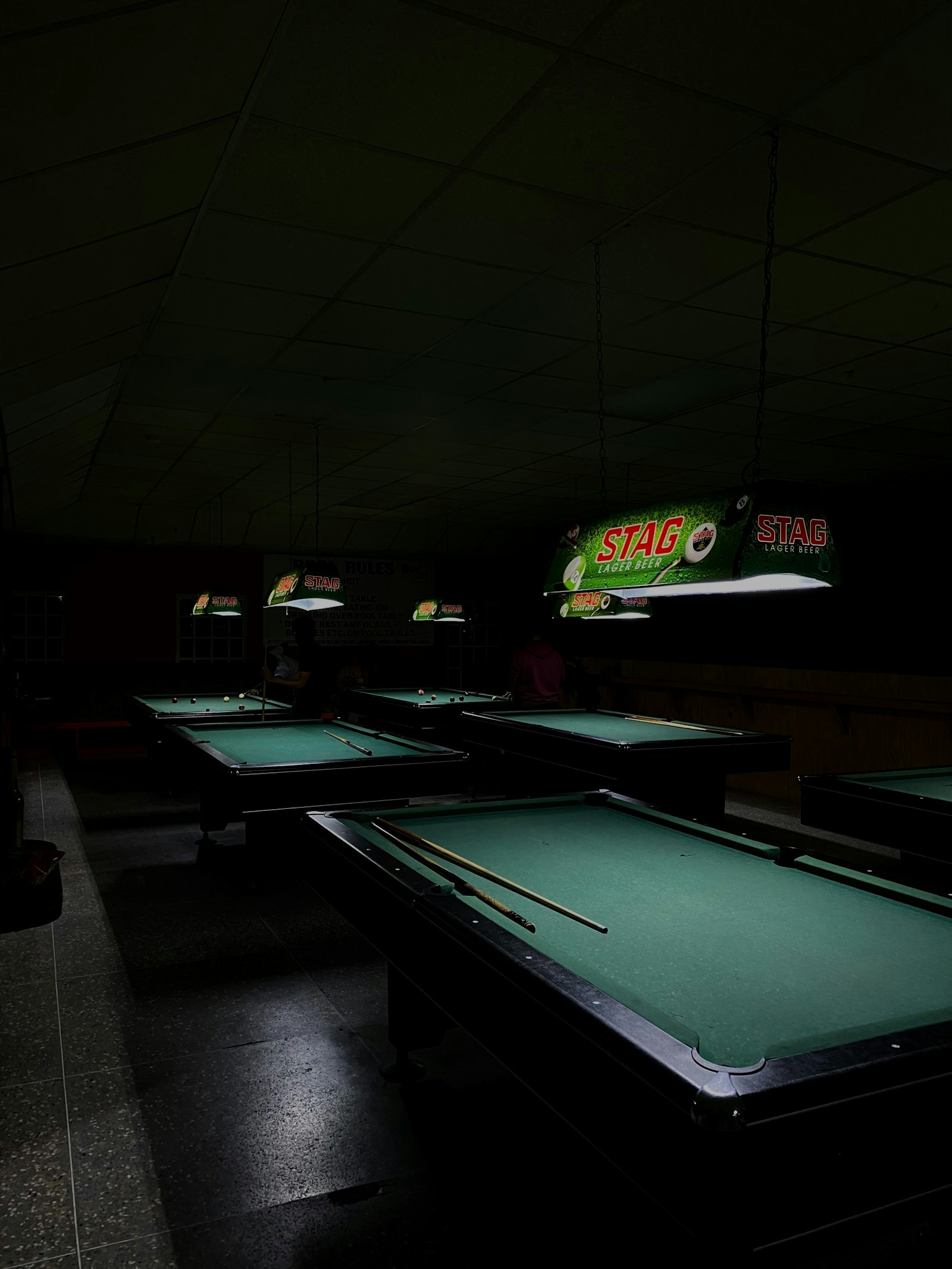 Rows of green pool tables in a dark pool hall.